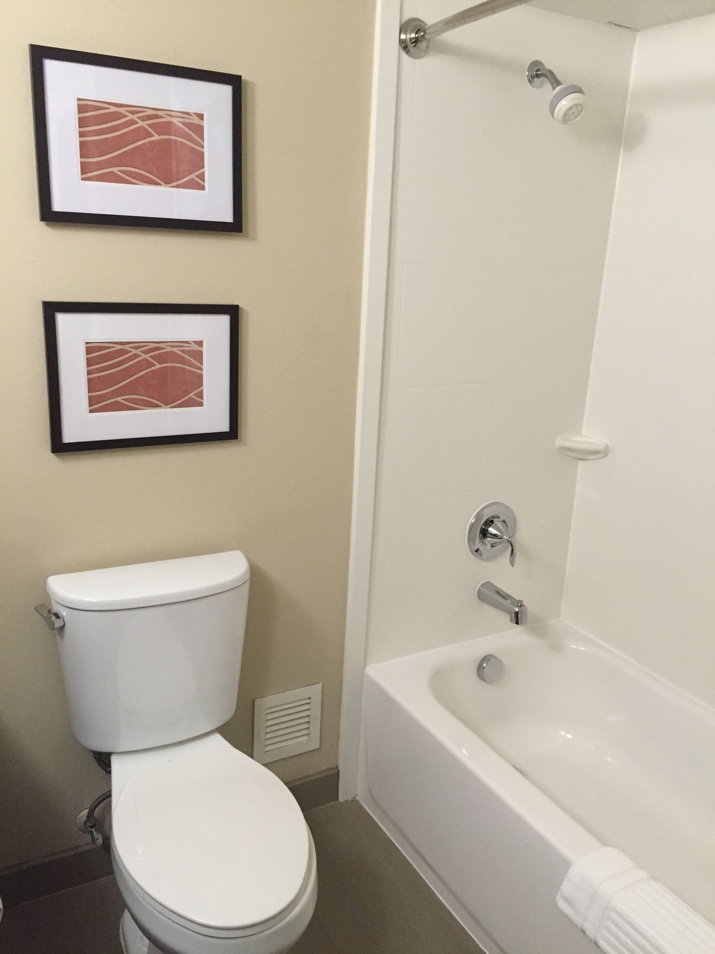 Une salle de bain avec des toilettes, une baignoire et deux tableaux encadrés au mur.