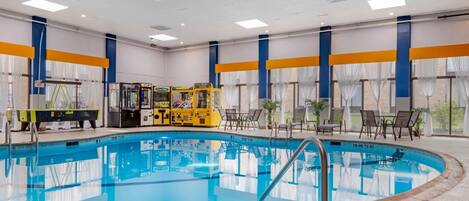 Una gran piscina interior con agua cristalina, rodeada de sillones de descanso y una zona de juegos para niños.