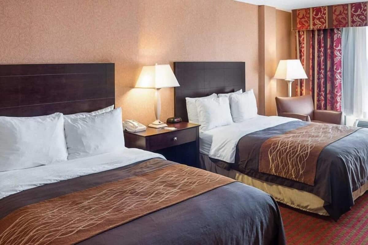 A hotel room with two beds, nightstands, lamps, a chair, and a patterned carpet.
