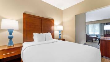 Habitación de hotel con una cama grande, dos mesitas de noche con lámparas, un cabecero de madera y vistas al área del vestíbulo del hotel.