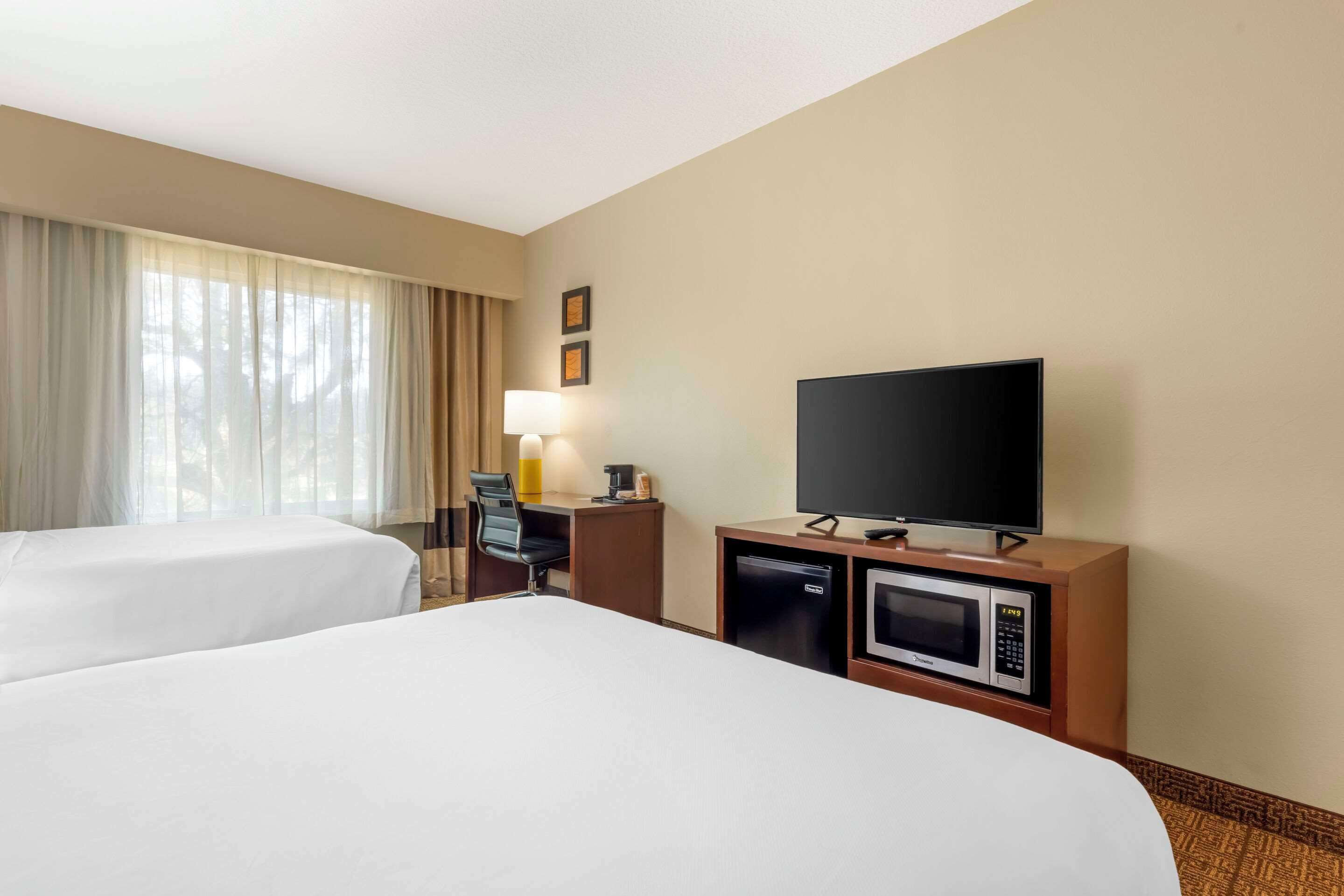 Habitación de hotel con dos camas, un escritorio con lámpara, televisión, microondas y refrigerador pequeño.
