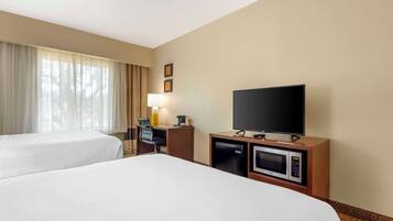 Habitación de hotel con dos camas, un escritorio con lámpara, televisión, microondas y refrigerador pequeño.