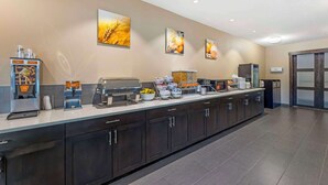 Una larga barra de buffet con diferentes estaciones de comida, incluyendo una máquina de café y un bol de fruta.