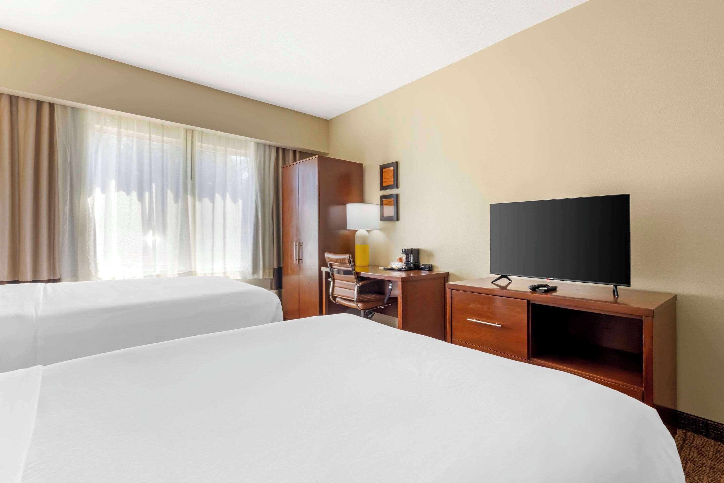 A hotel room with two beds, a desk, a television, and a window with curtains.