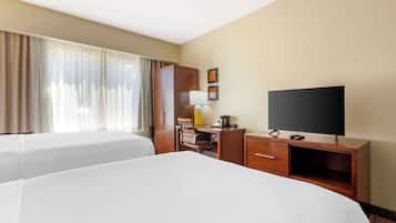 A hotel room with two beds, a desk, a television, and a window with curtains.