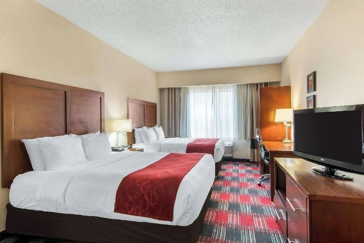 A hotel room with two beds, a TV, a desk, and a window with curtains.