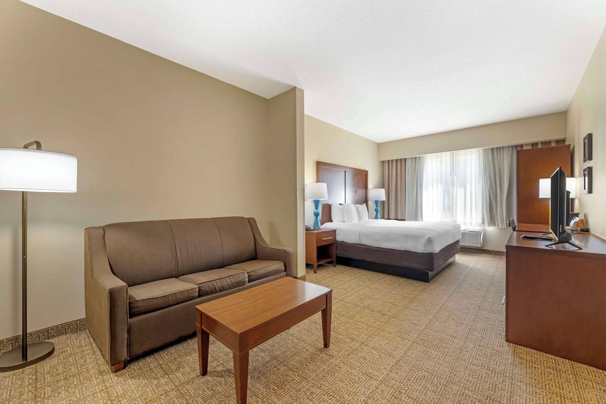 Una habitación de hotel con sofá, cama, escritorio y lámpara.