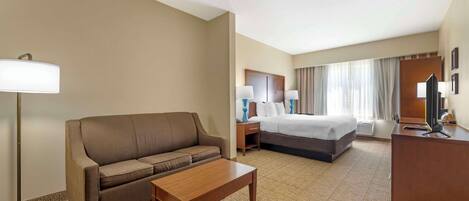 A hotel room with a sofa, a bed, a desk, and a lamp.