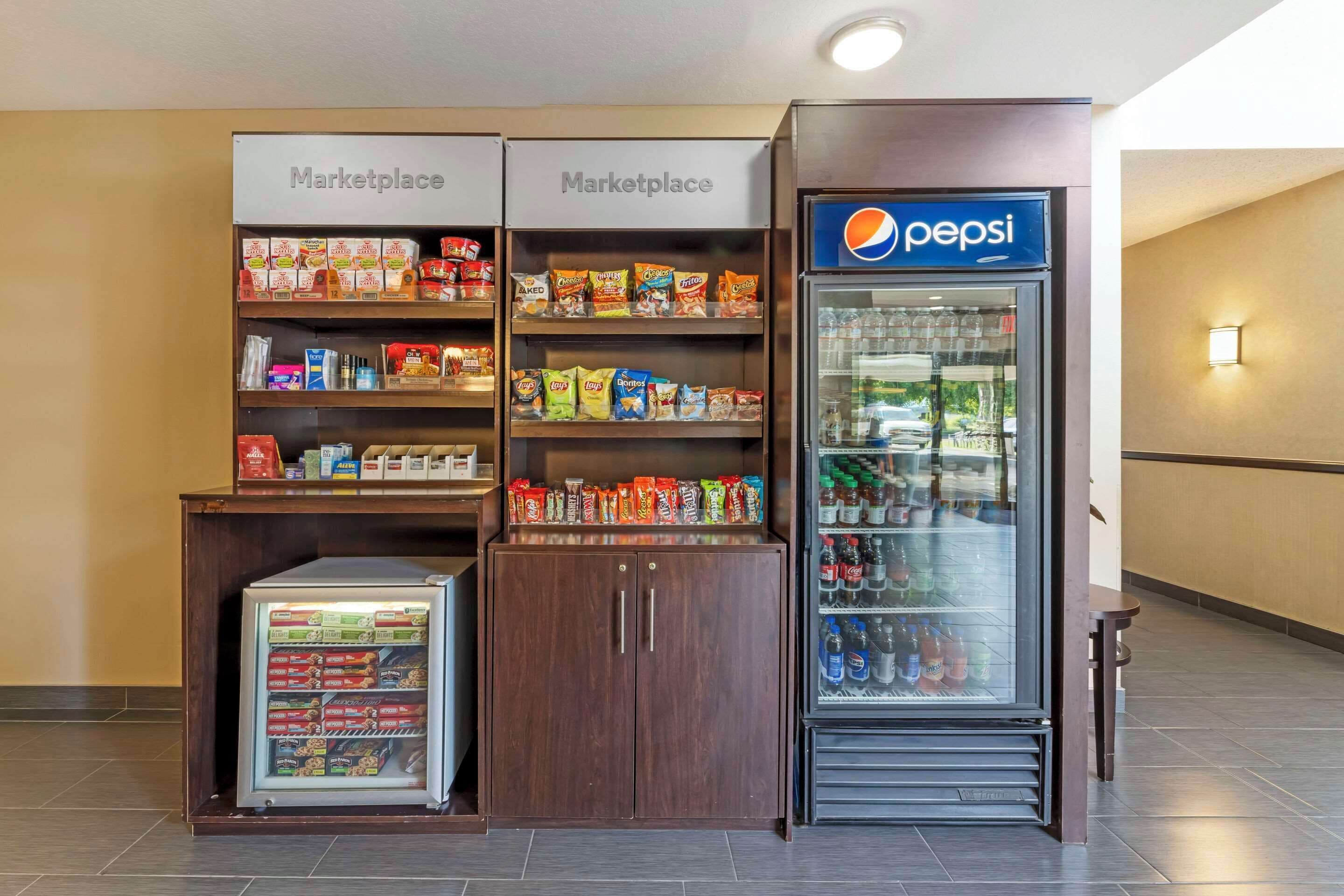 A kitchenette area with two refrigerators, a vending machine, and shelves stocked with snacks and beverages.
