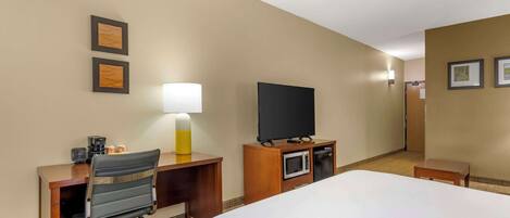 A hotel room with a bed, desk, chair, television, microwave, and lamp.