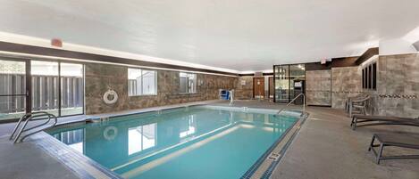 Una piscina interior con agua cristalina, bordes azulejados y una silla para salvavidas.