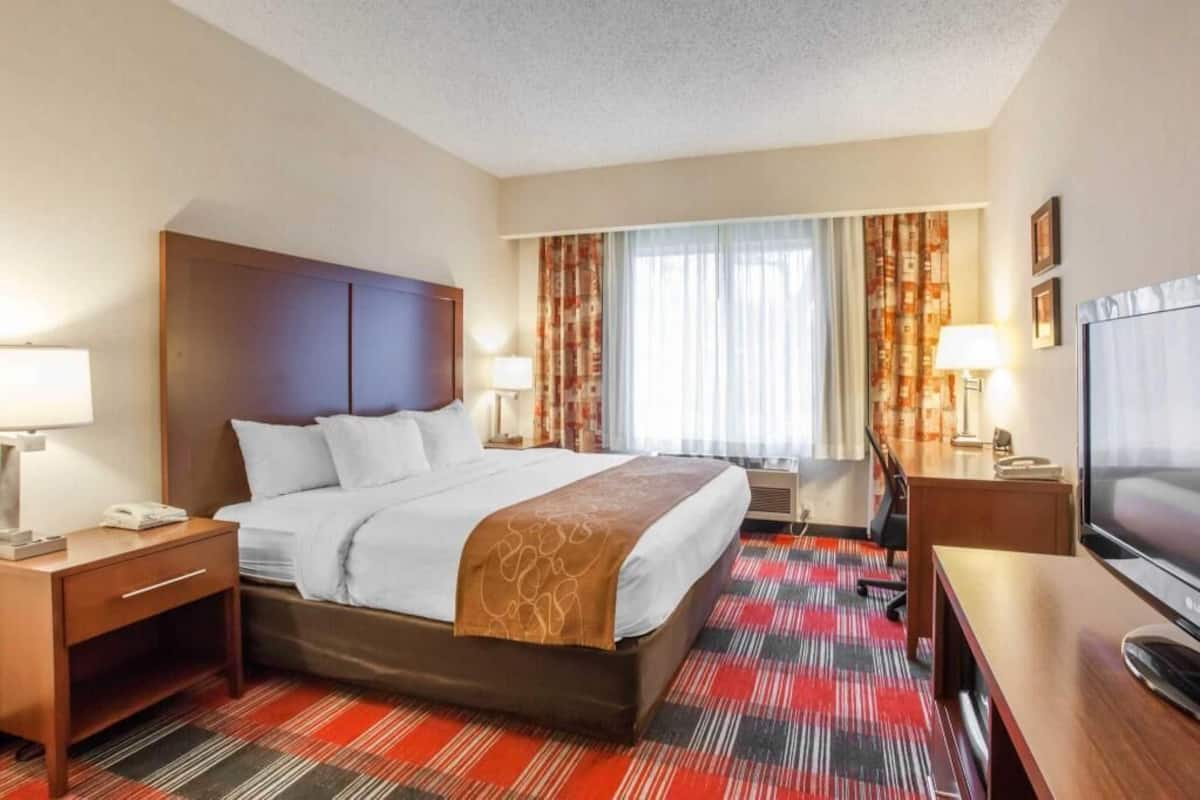 Une chambre d’hôtel comprenant un lit, des tables de chevet, un bureau, une télévision et une fenêtre avec des rideaux.