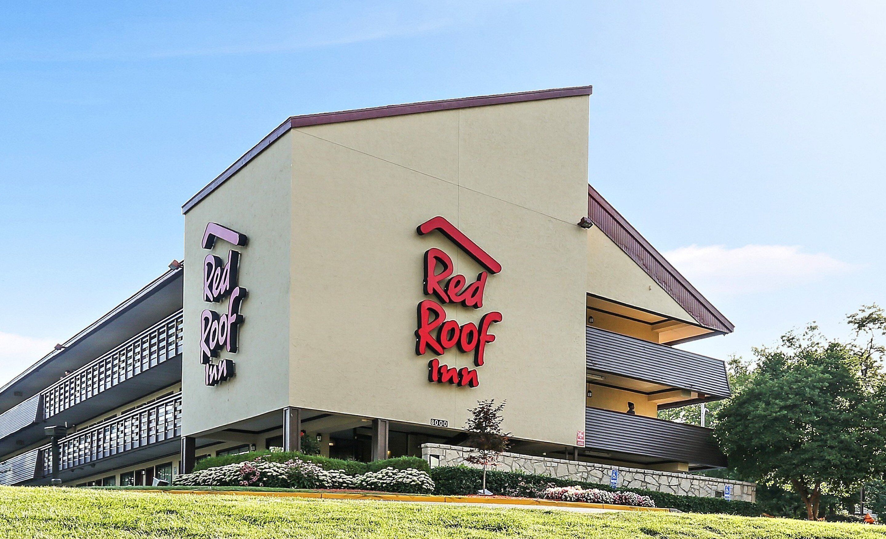 A Red Roof Inn building with a modern architectural design, featuring a prominent red roof sign and a two-story structure with balconies.