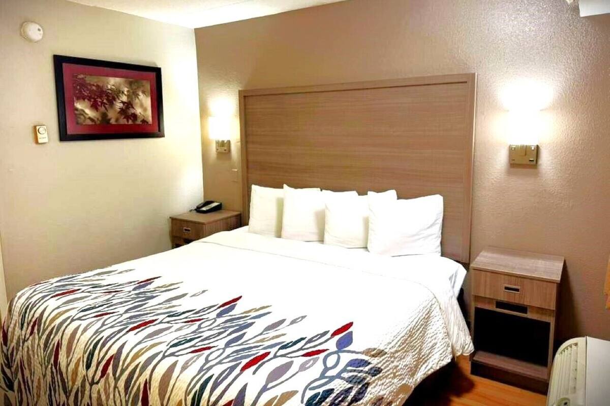 A hotel room with a large bed, a nightstand, a bedside table, and a wall-mounted light.