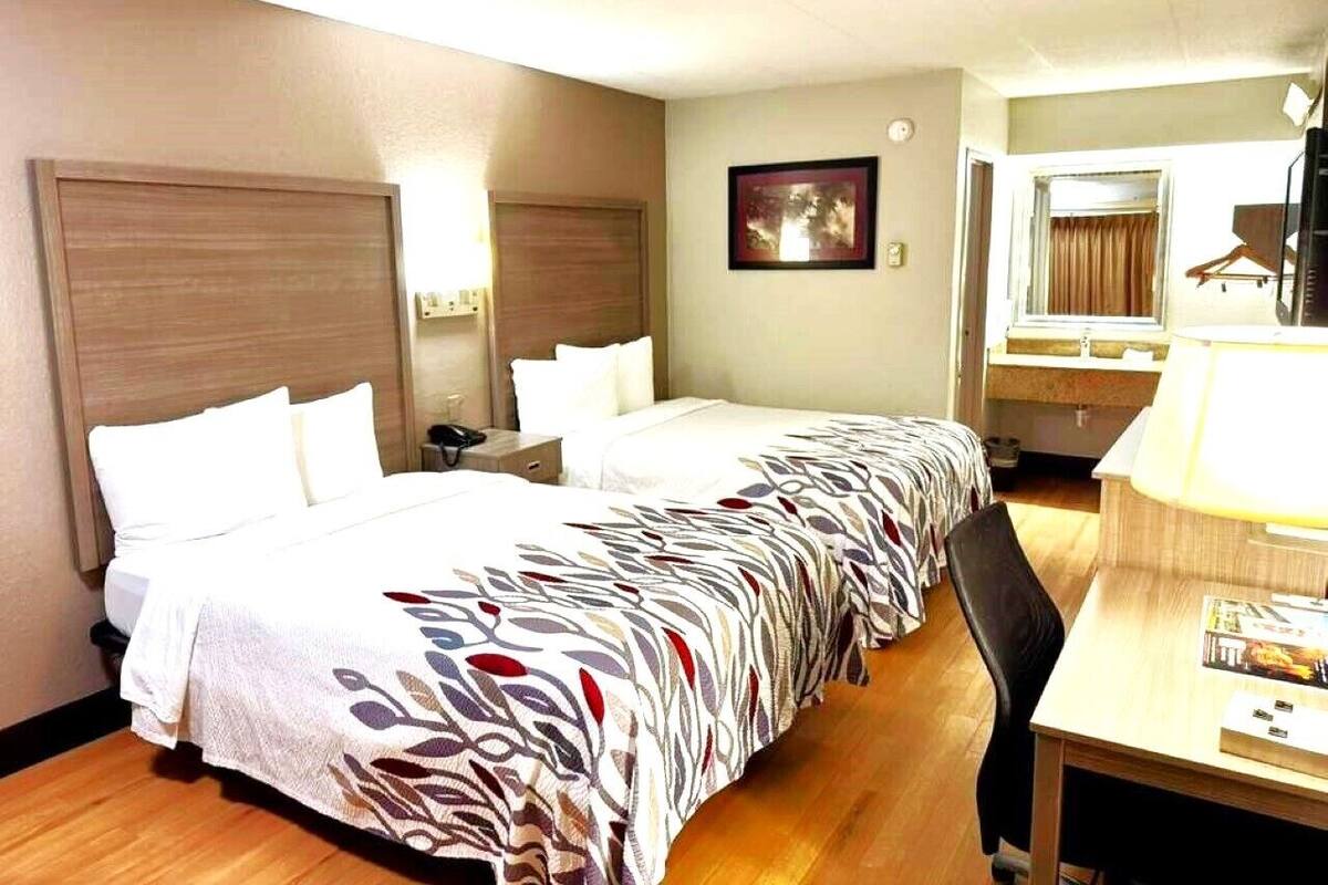 A hotel room with a large bed, a desk, a chair, a mirror, and a picture on the wall.