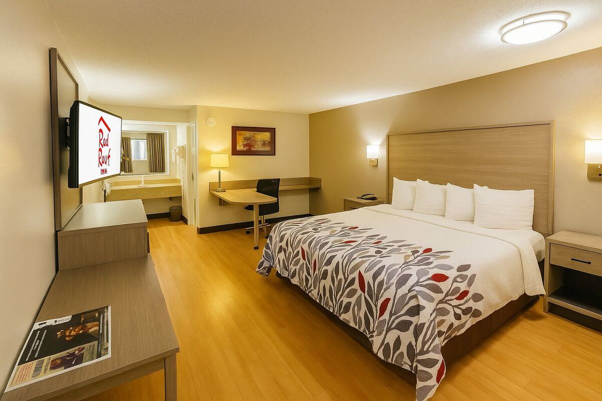 A hotel room with a bed, a desk, a chair, a lamp, and a TV.