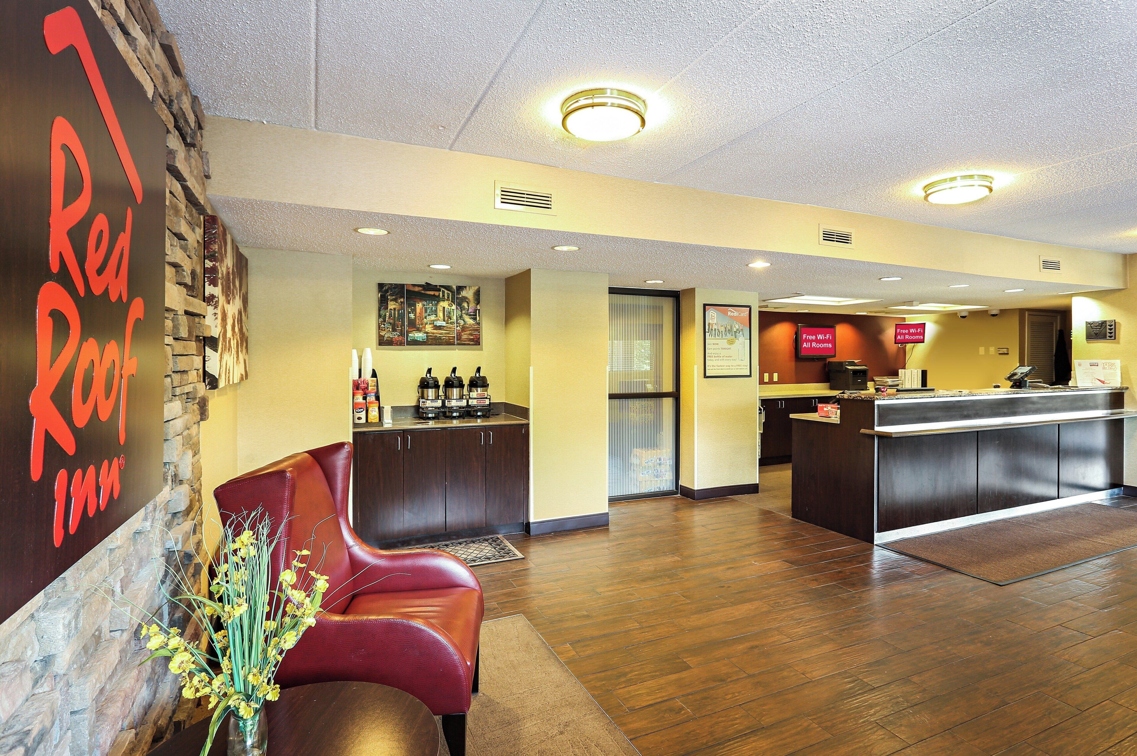 A hotel lobby with a reception desk, a seating area with a red leather couch, and a wall with a 'Red Roof Inn' sign.