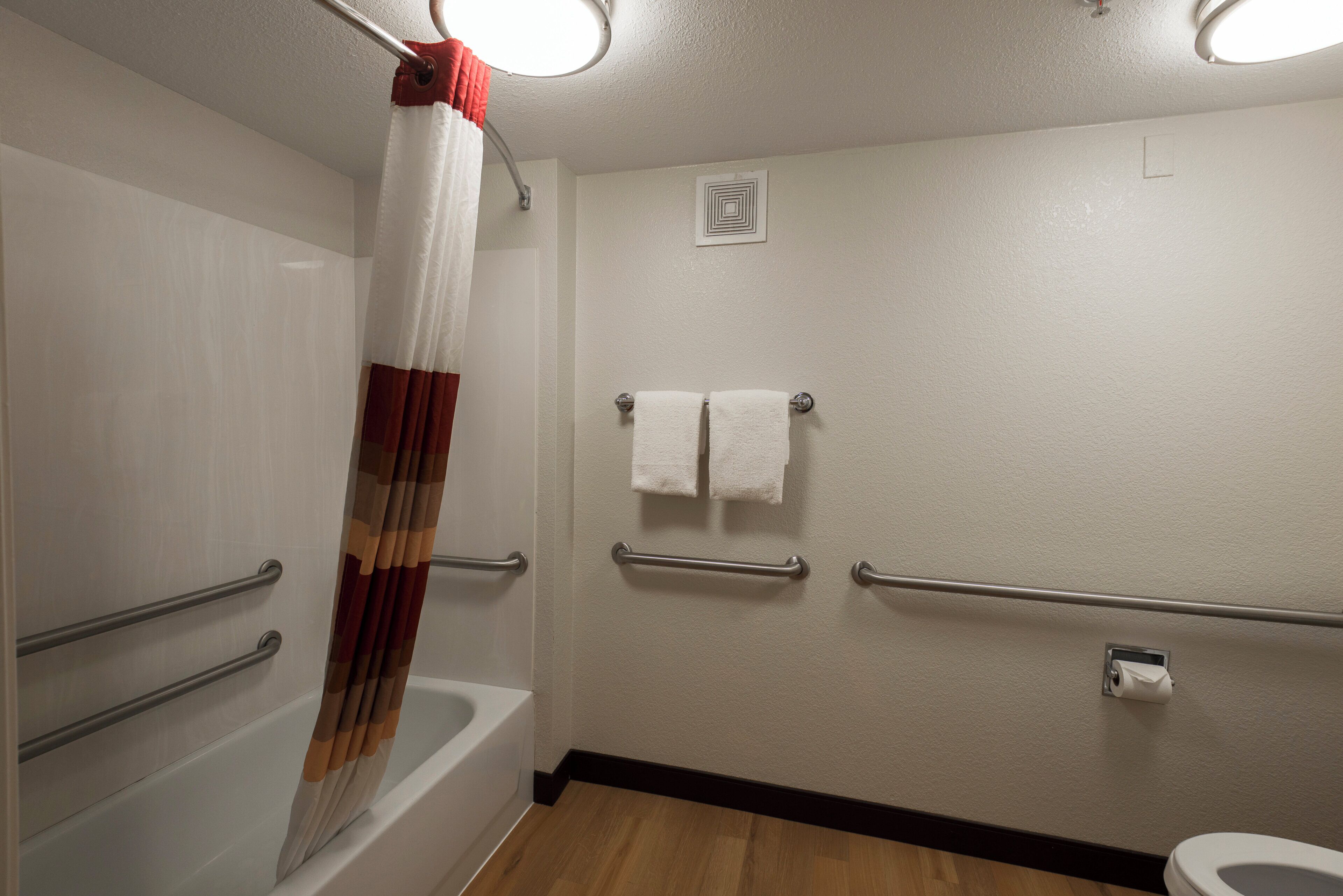 A bathroom with a bathtub, a shower curtain, a toilet, and handrails.