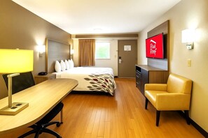 A hotel room with a bed, desk, chair, TV, and a door.