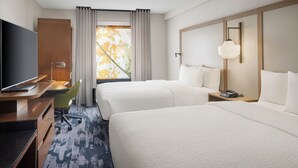 Een hotelkamer met twee bedden, een bureau met een televisie, een stoel, een lamp en een raam met gordijnen.