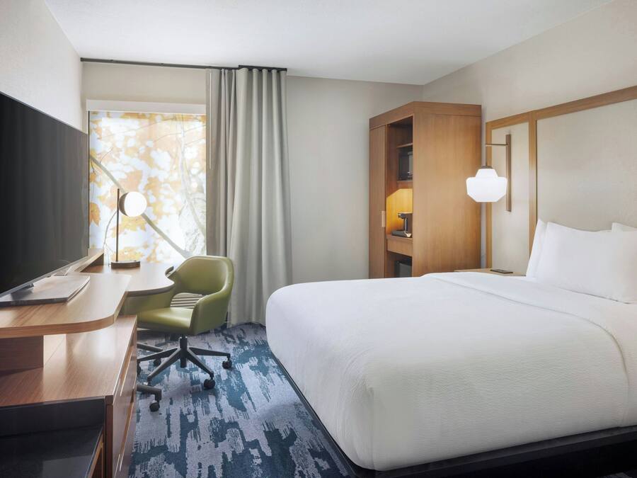 Ein Hotelzimmer mit einem großen Bett, einem Schreibtisch mit Flachbildfernseher, einem grünen Sessel und einem Nachttisch mit Lampe.