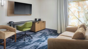 Hotelkamer met een flatscreen televisie aan de muur, een houten bureau met stoel, een bank en een groot raam met gordijnen.