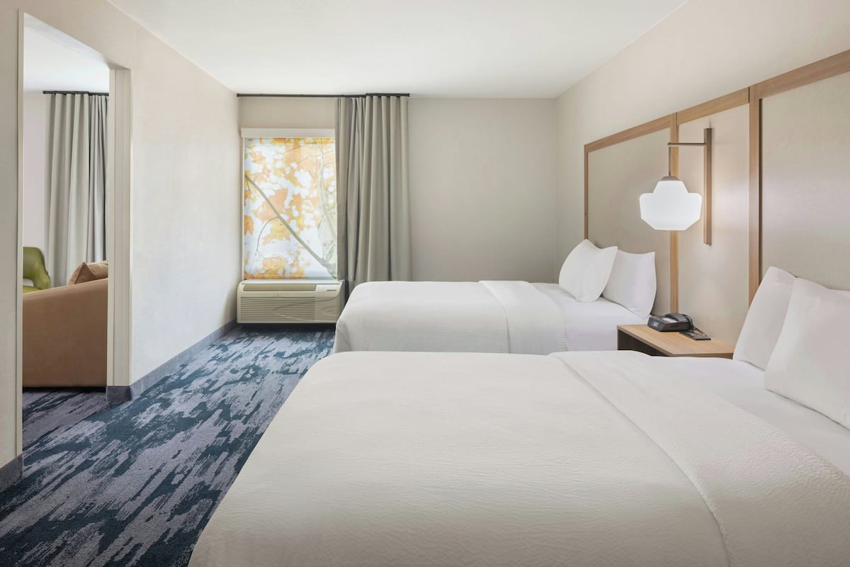 Ein Hotelzimmer mit zwei Betten, einem großen Fenster mit Vorhängen, einer Wandlampe und einem Nachttisch mit Telefon.