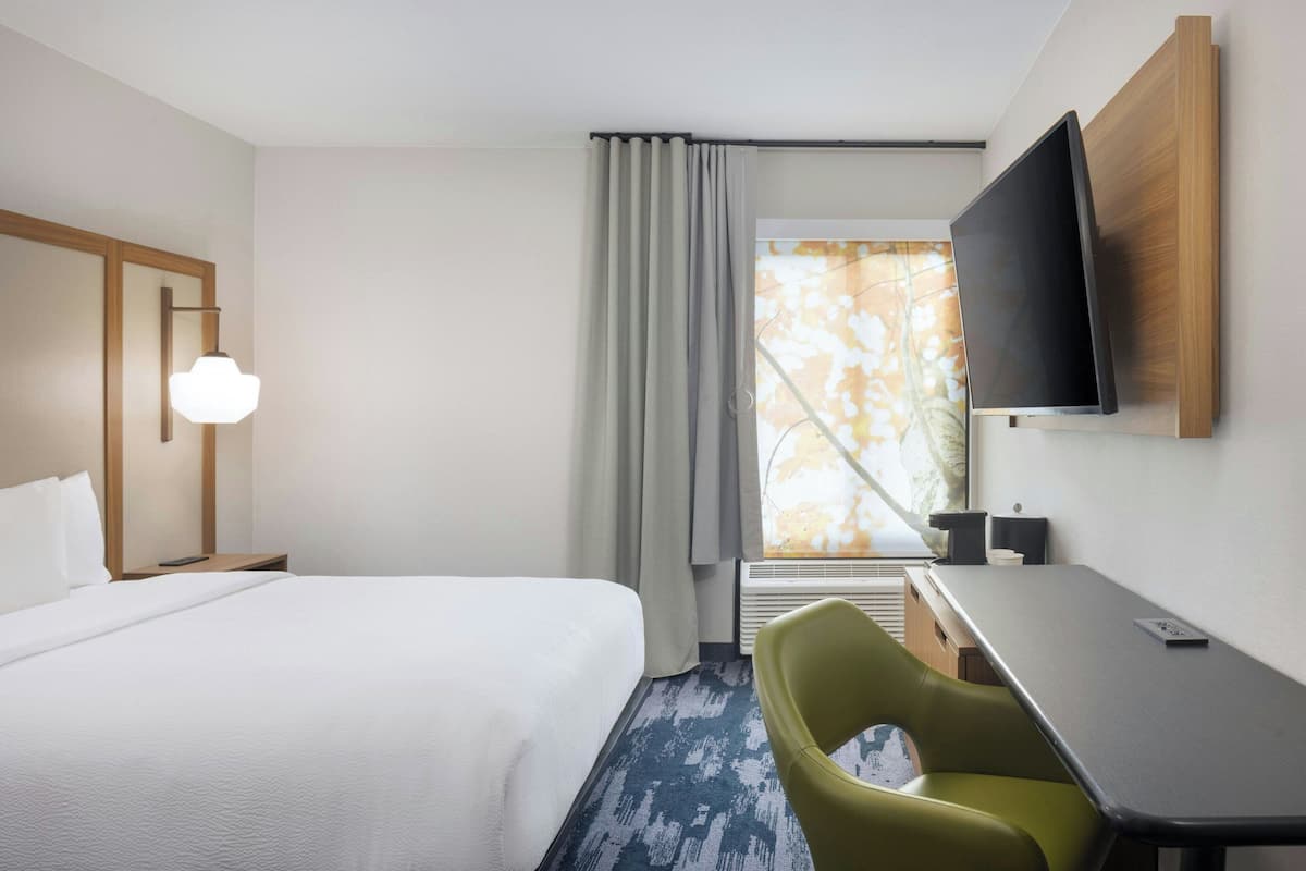 Ein Hotelzimmer mit einem Bett, einem Schreibtisch, einem Stuhl, einem Fernseher und einem Fenster mit Vorhängen.