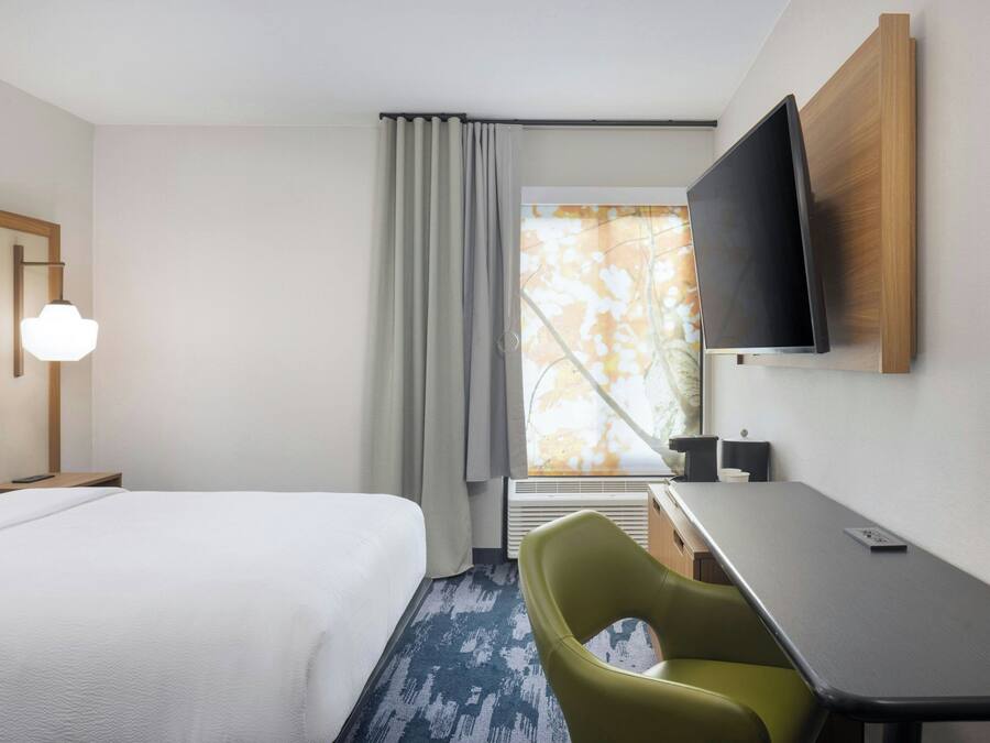 Habitación de hotel con cama, escritorio, silla, televisor y ventana con cortinas.