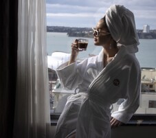 Una persona con bata blanca sentada junto a una ventana con vista al agua y edificios.