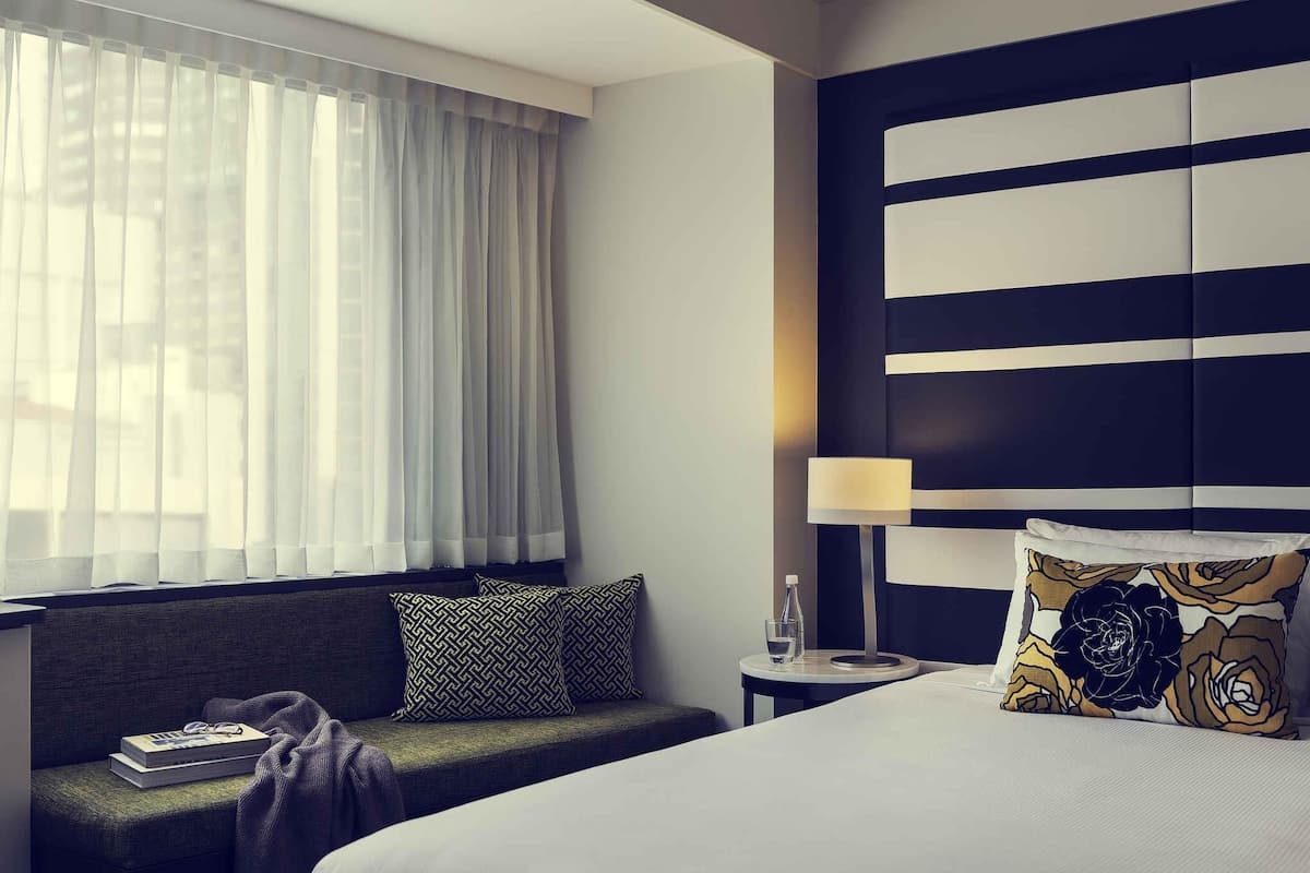 A hotel room with a bed, a sofa, a nightstand, a lamp, and a window with curtains.