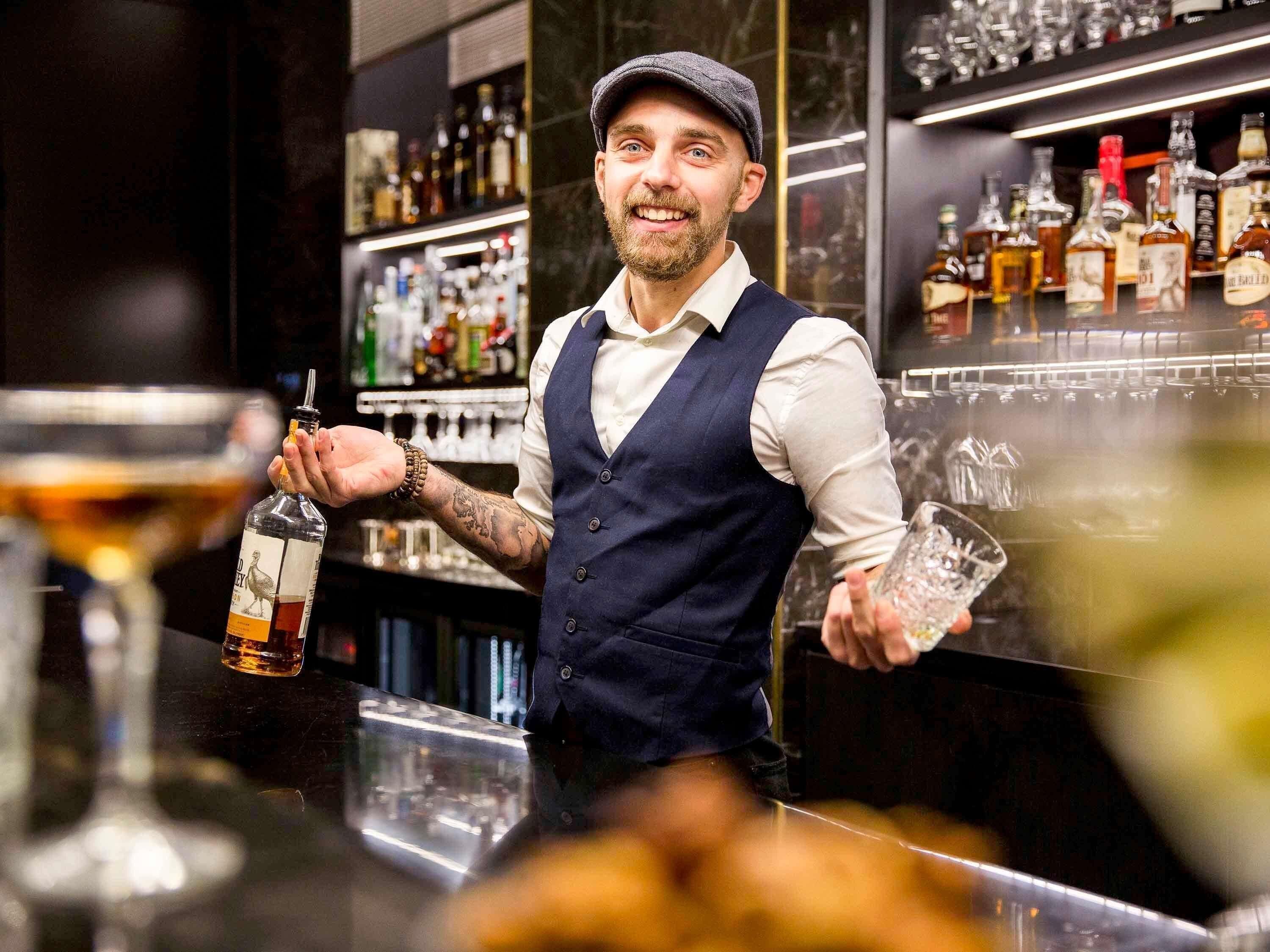 A bartender holding a bottle and a glass, with shelves of bottles in the background.