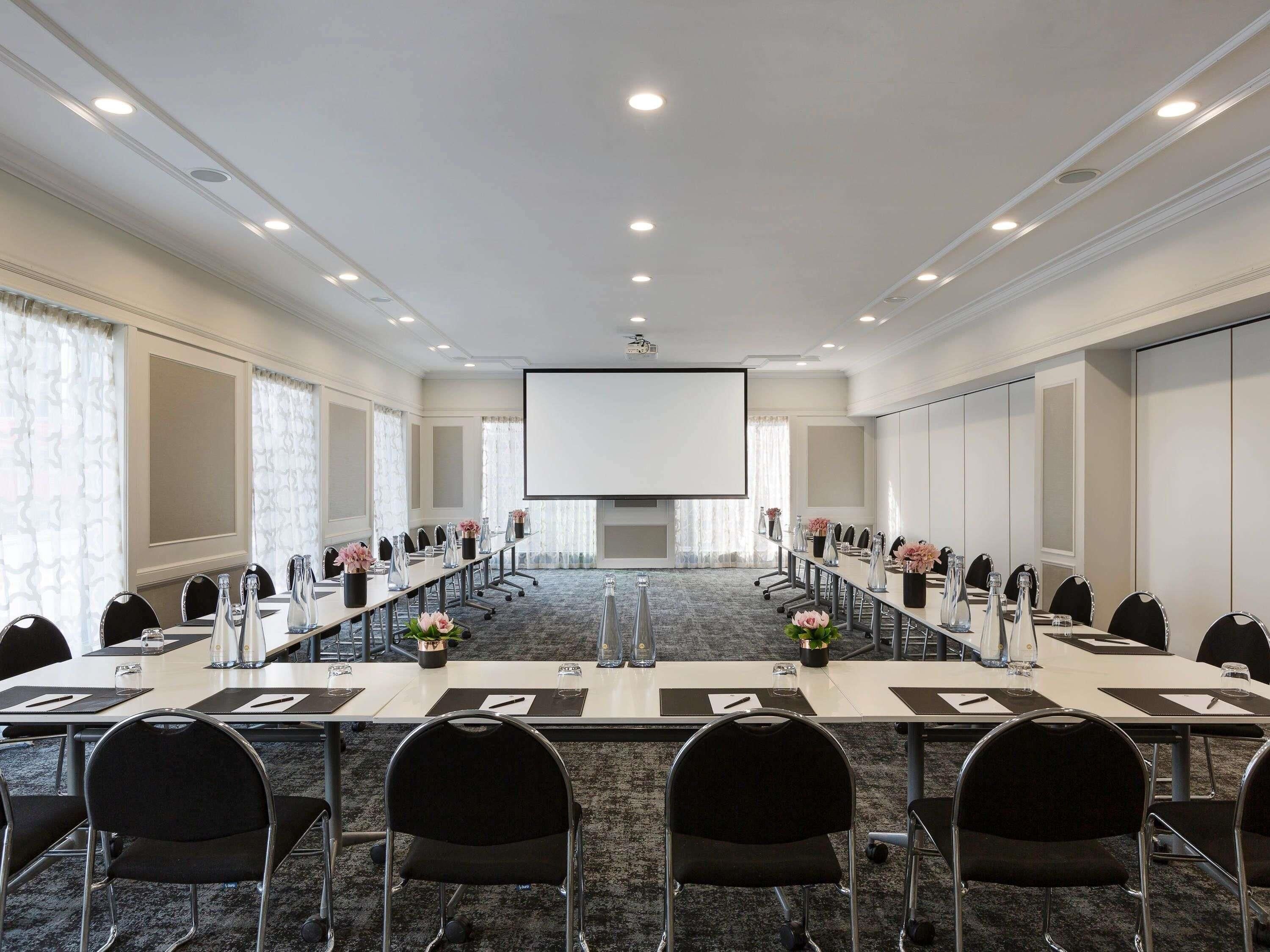 A conference room with a long table, chairs, a projector screen, and a carpeted floor.