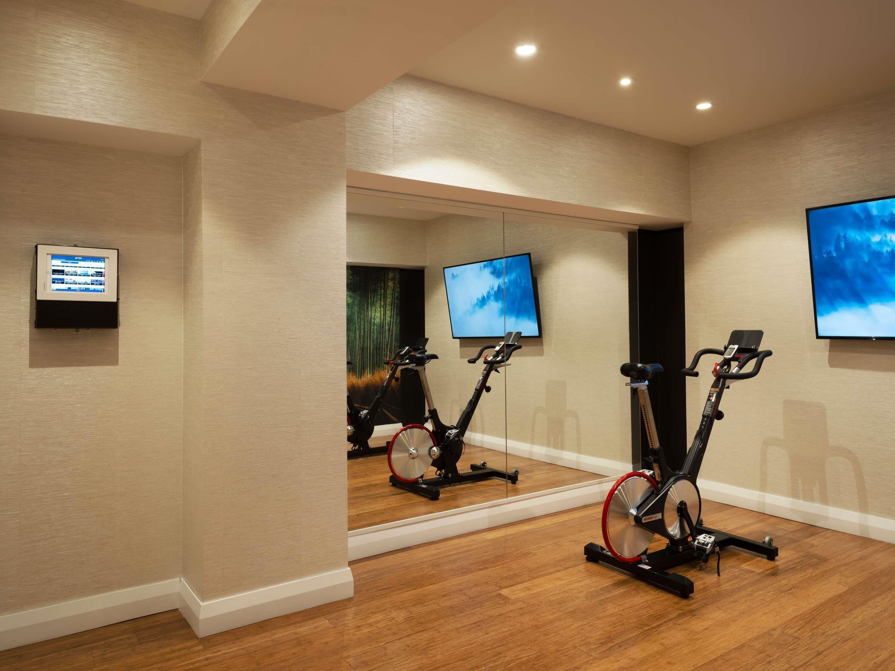 Une salle de sport équipée de vélos d’appartement, d’un grand miroir et d’un téléviseur fixé au mur.