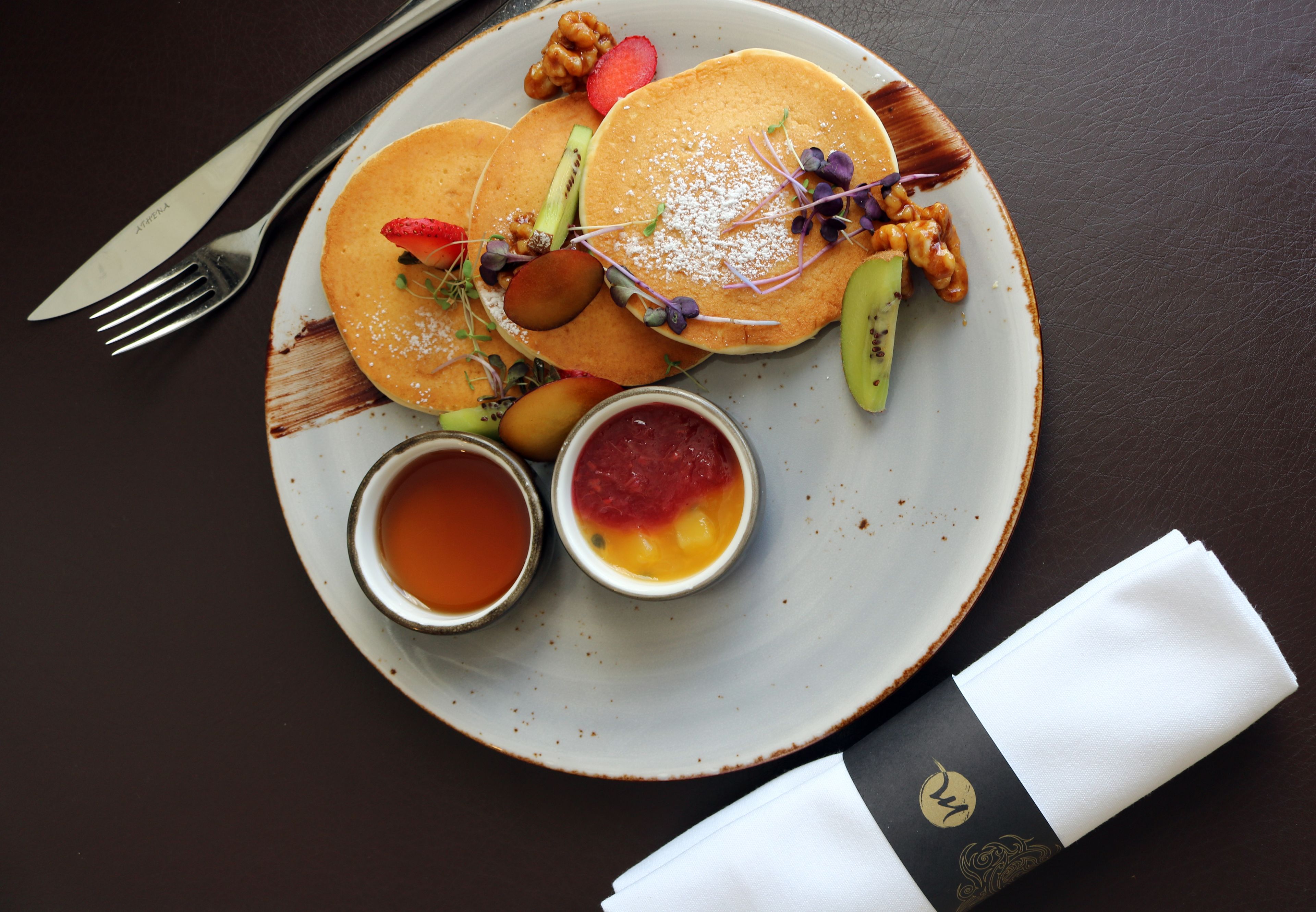 A plate of pancakes with various toppings and two small bowls of syrup.