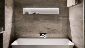 A modern bathroom with a freestanding bathtub, marble walls, and a built-in shelf with toiletries.