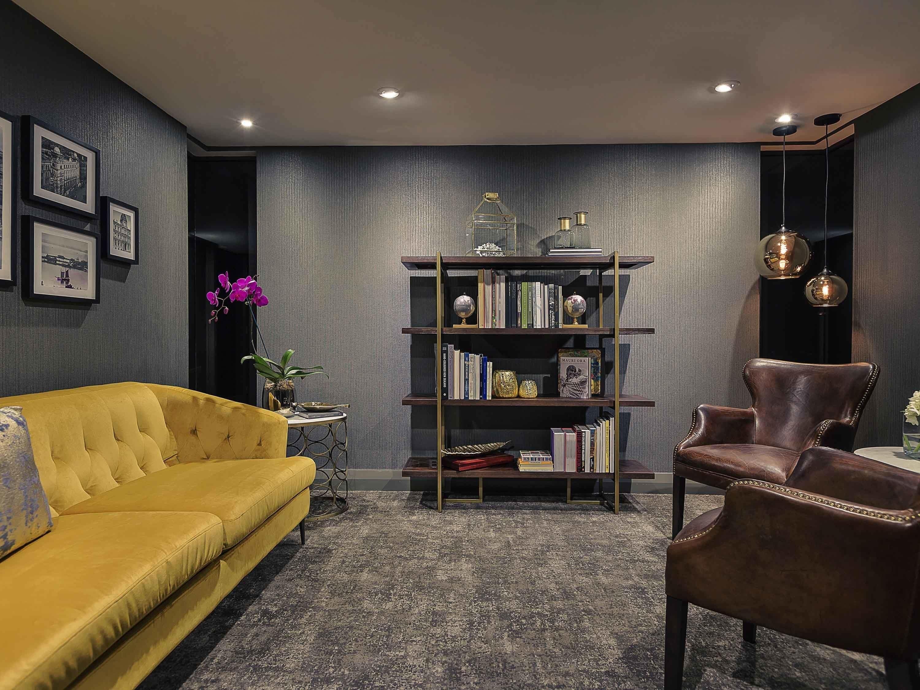 A modern living room with a yellow sofa, a leather armchair, a bookshelf, and a small side table with a potted plant.