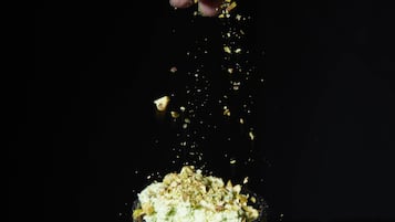 A hand sprinkling a powdery substance over a layered dessert in a clear glass.