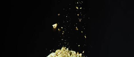 A hand sprinkling a powdery substance over a layered dessert in a clear glass.