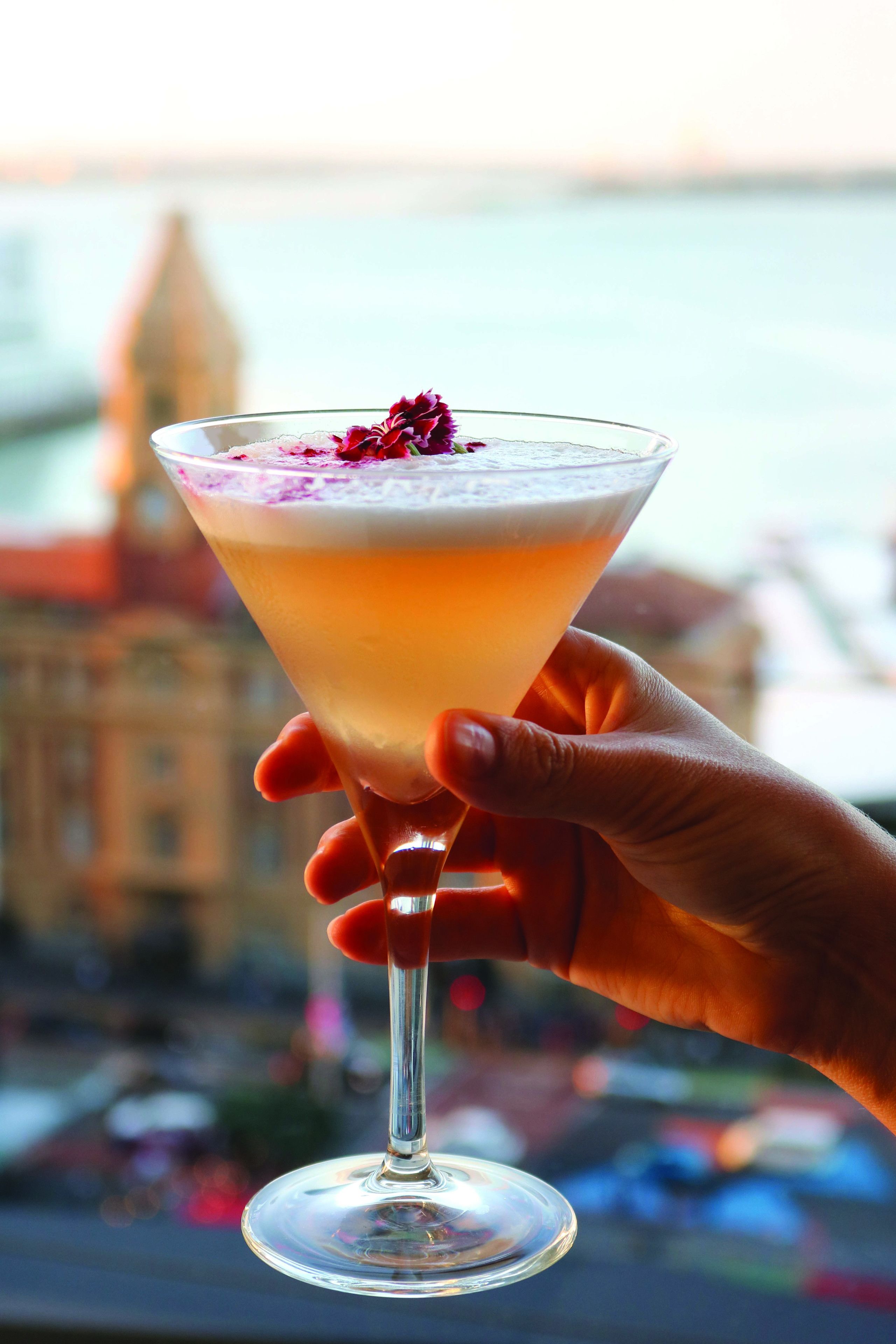 A cocktail in a martini glass with a garnish, held by a hand.