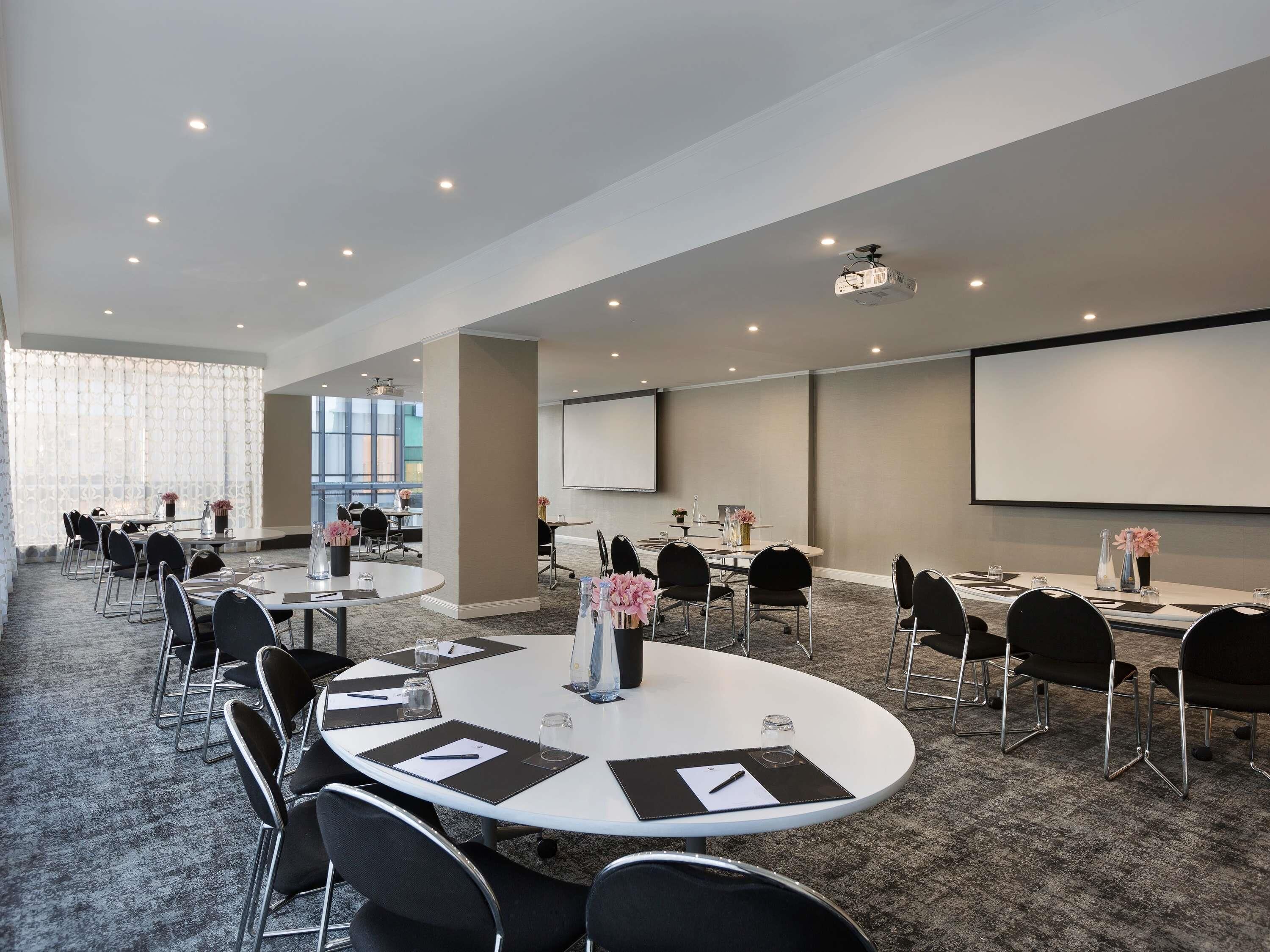A conference room with round tables, black chairs, a projector, and a screen.