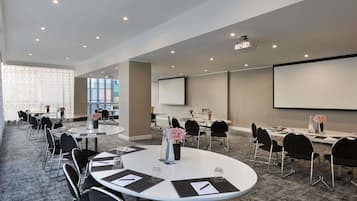 A conference room with round tables, black chairs, a projector, and a screen.