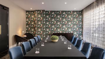 A conference room with a long table, blue chairs, a floral wallpaper, and a piano.