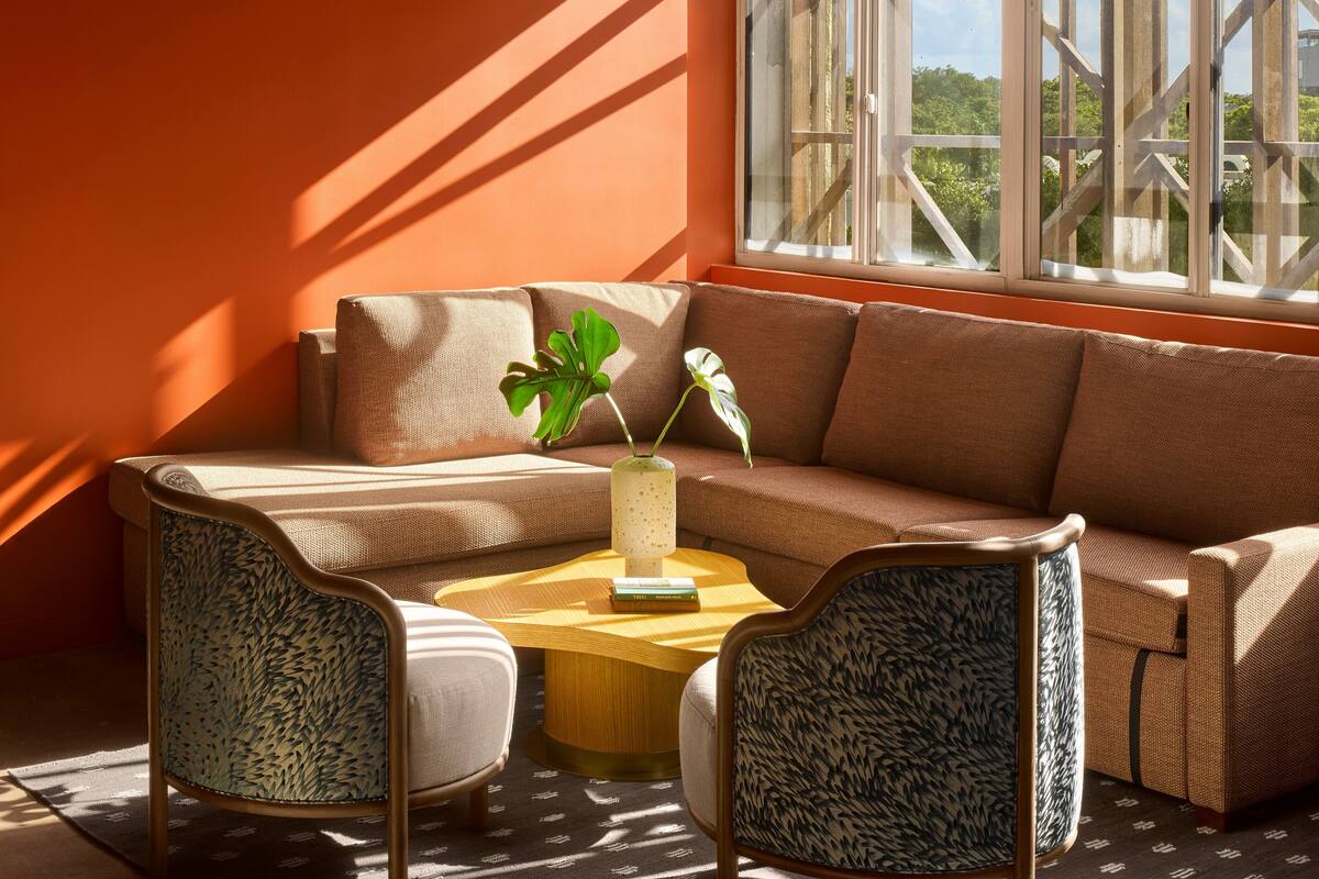 A modern living room with a brown sofa, two patterned chairs, a wooden coffee table, and a plant.
