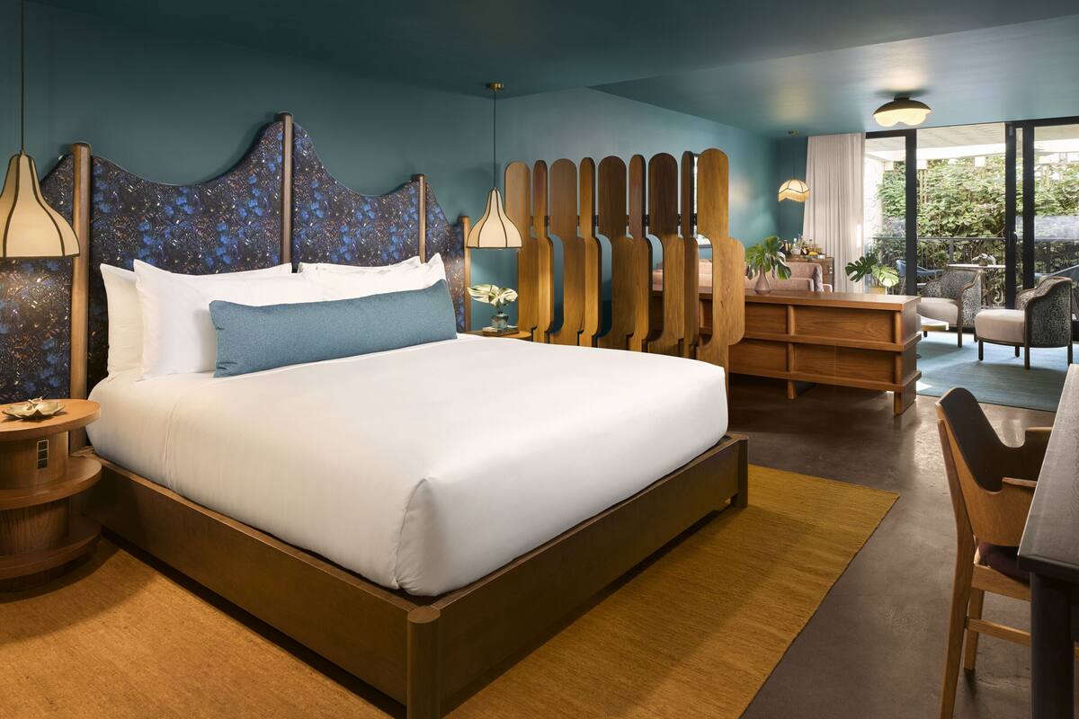 A modern hotel room with a large bed, wooden headboard, and a view of the outdoors.