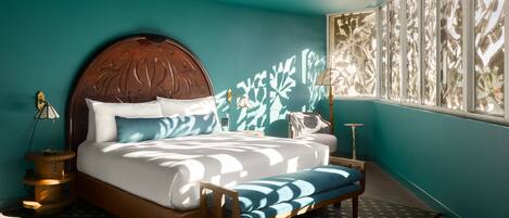 A bedroom with a large bed, a wooden headboard, a patterned rug, and a window with a view of trees.