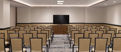 A conference room with rows of chairs, a large flat-screen TV, and a patterned carpet.