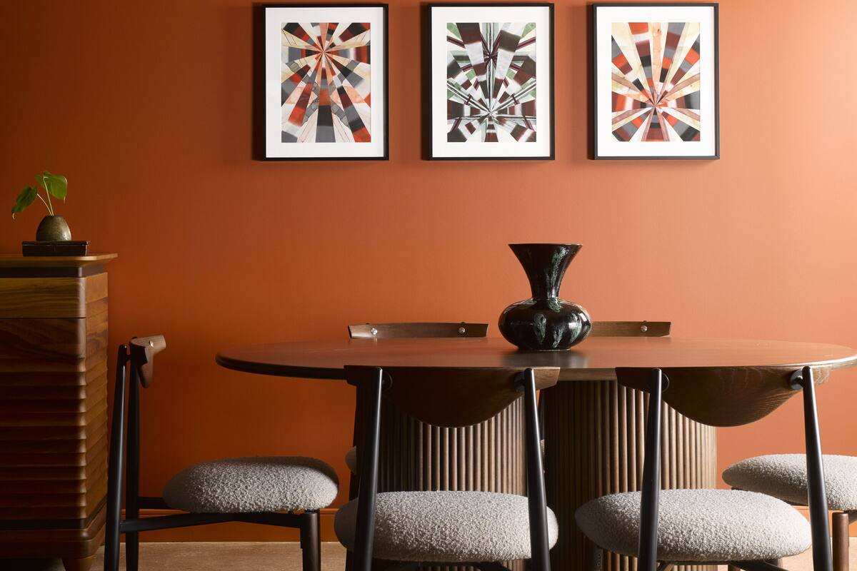 A dining area with a round table, four chairs, and three framed abstract art pieces on the wall.
