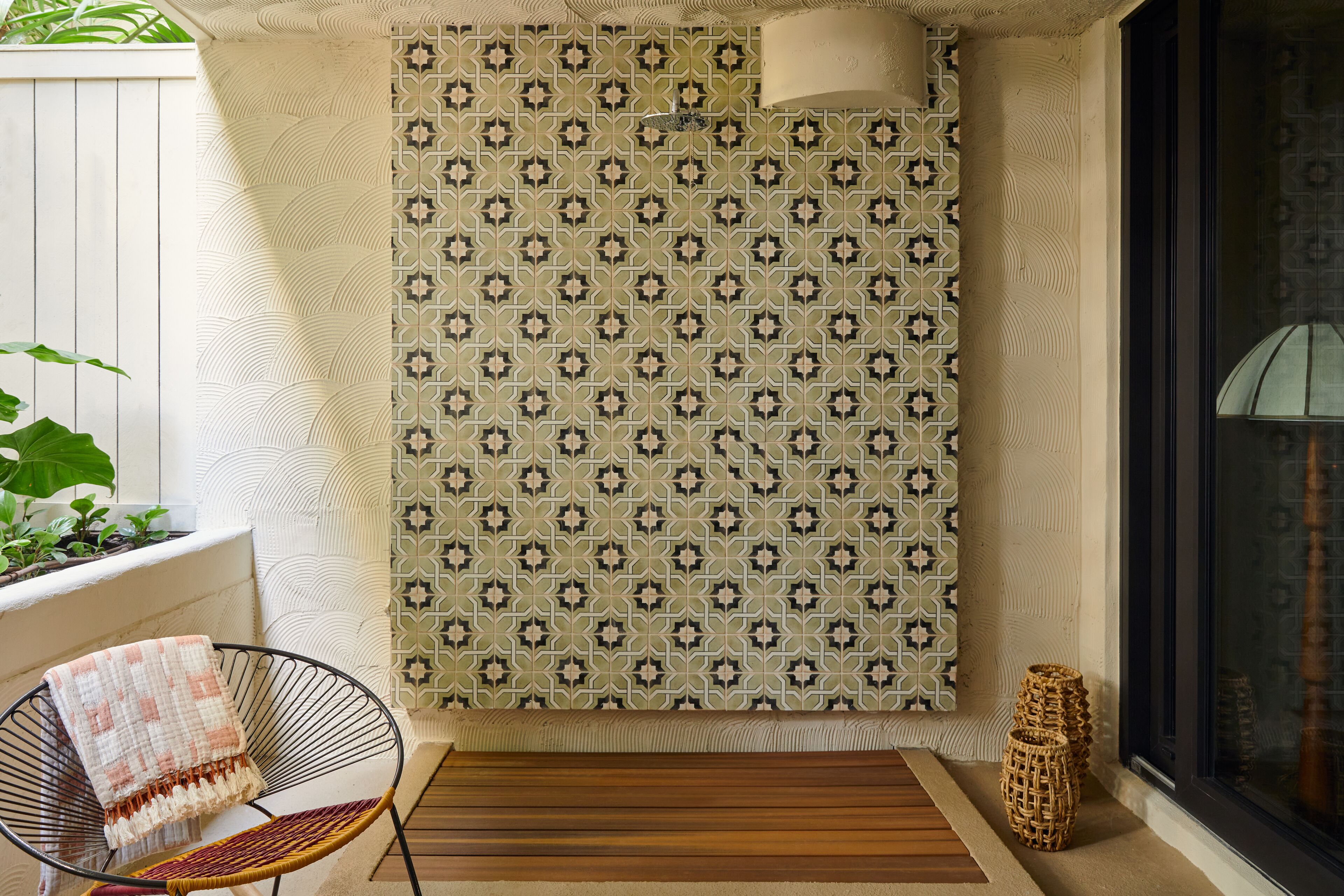 Un coin de pièce avec un papier peint à motifs, une chaise recouverte d’une couverture et un petit banc en bois.