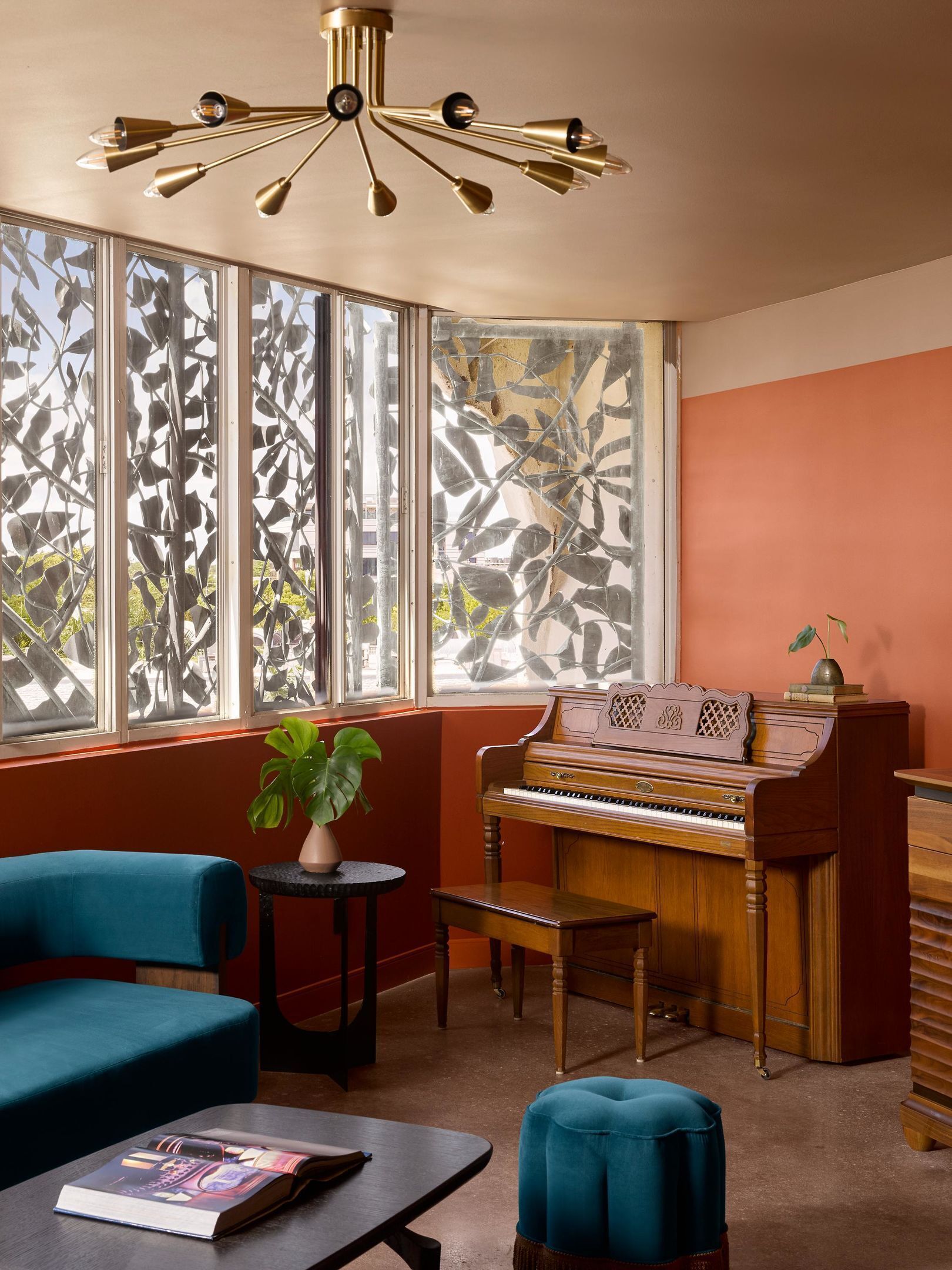 Una habitación con un piano, un sofá azul, una mesita con un libro y una planta.